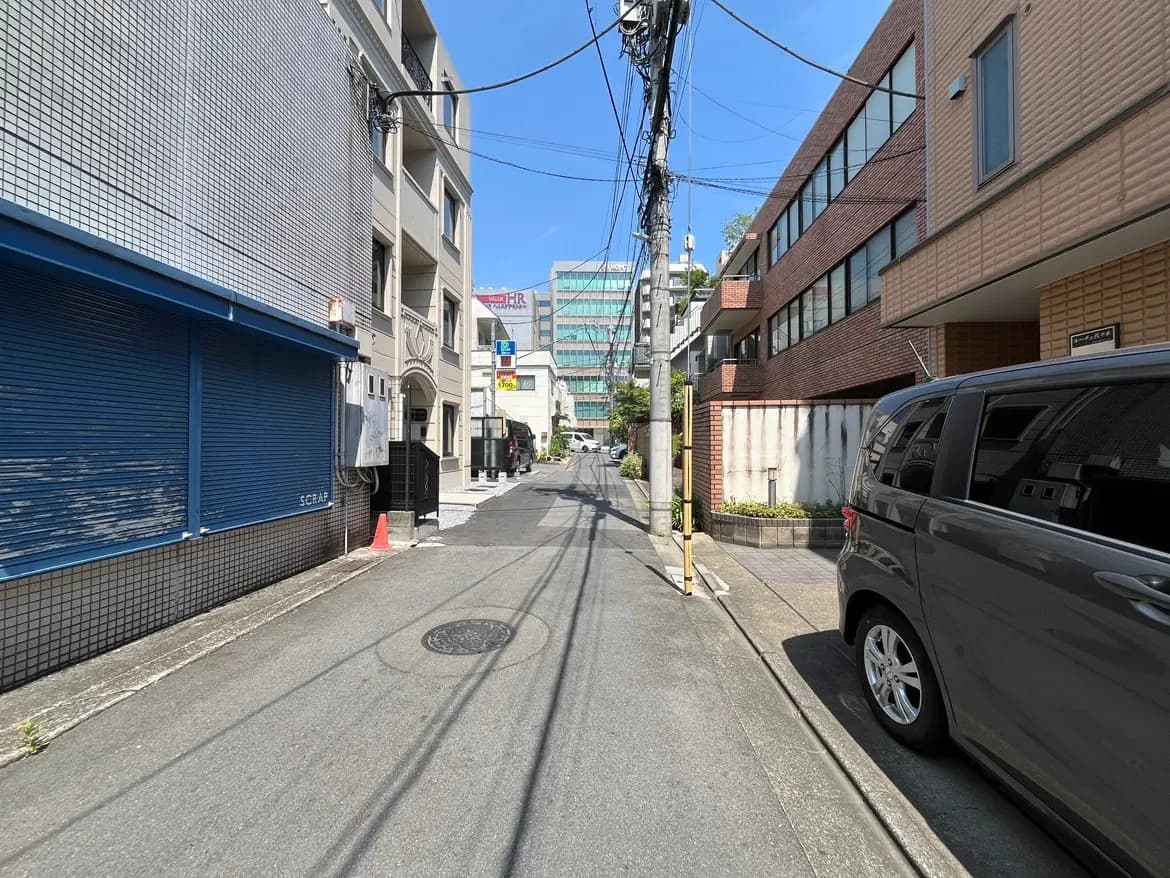 - 都市の静かな裏道、青いシャッターの店舗とレンガ造りの建物が並び、青空が広がる風景