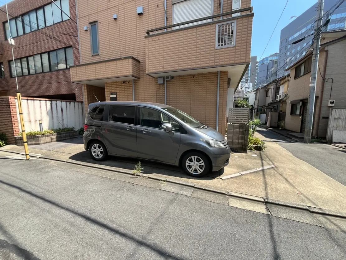 - 灰色のミニバンが住宅街の路肩に駐車されている風景、背景には近代的なビルと住宅が混在する街並み