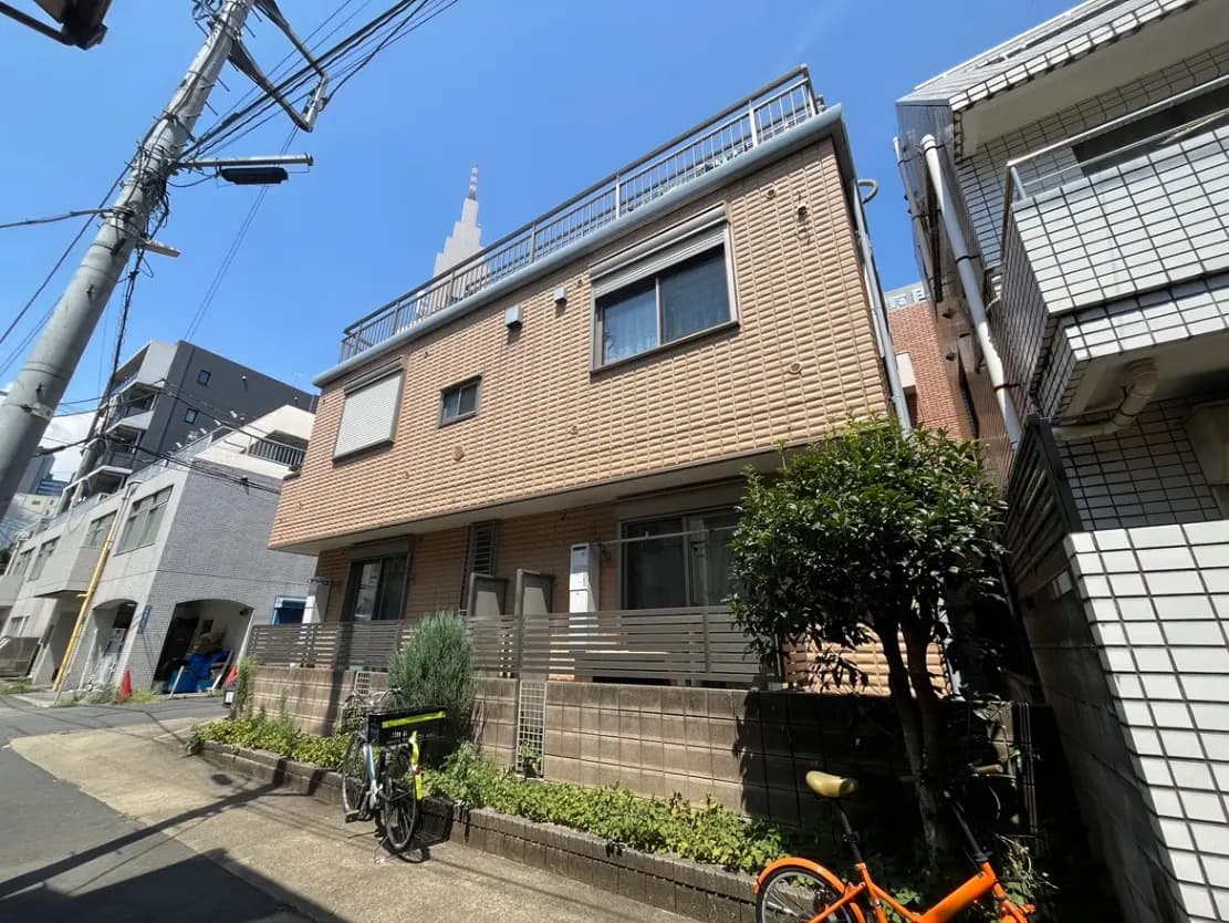 - 都市部にあるモダンな外観の住宅、青空を背景に、自転車と緑の植栽がある街並みの風景