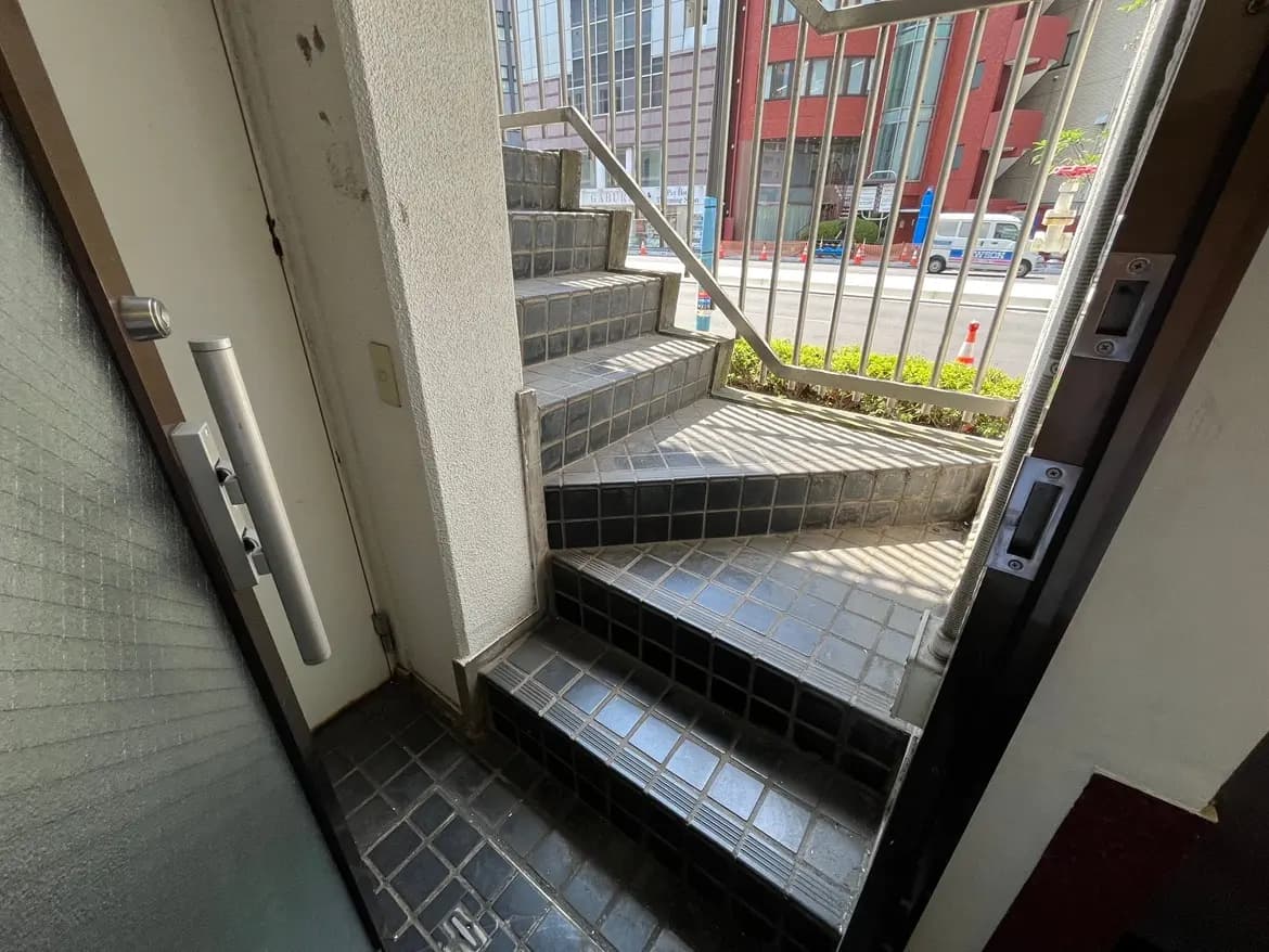 - 外階段に続く入口、白い壁と黒いタイルのステップが特徴的なアプローチ、街の風景が見える景色