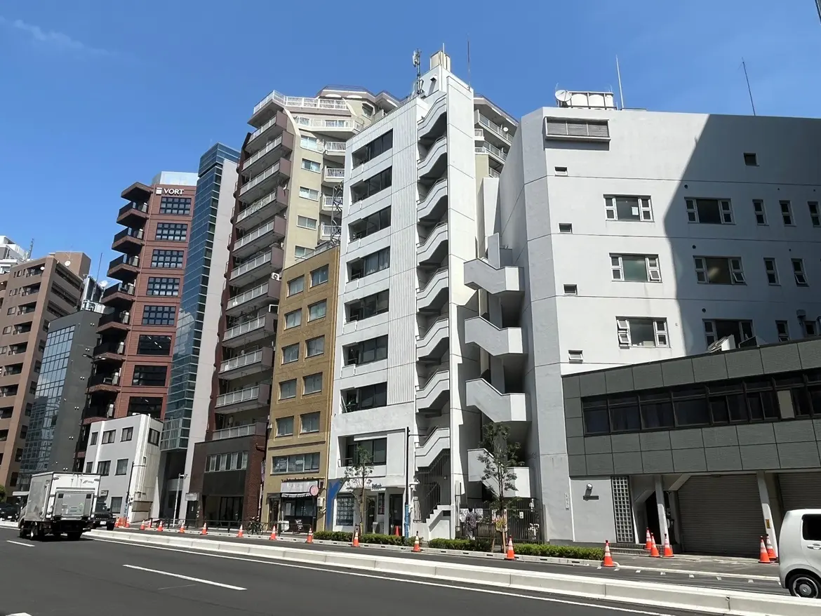 - 都市景観のビル群、様々な形状と色合いの建物が並ぶ街並み、明るい青空と交通の様子