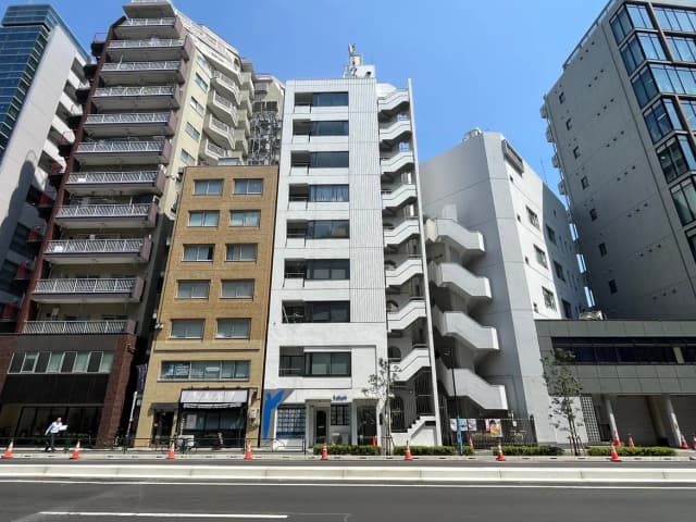 - 都市型のオフィスビルと住宅ビルの並ぶ街並み、青空が広がる中での建物ファサードの様子