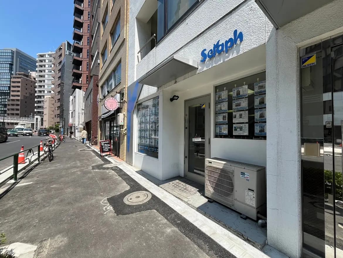 - 銀座のビル街に位置する不動産会社の店舗正面、ウィンドウに掲示された物件情報とエアコン設備が見える通りの風景