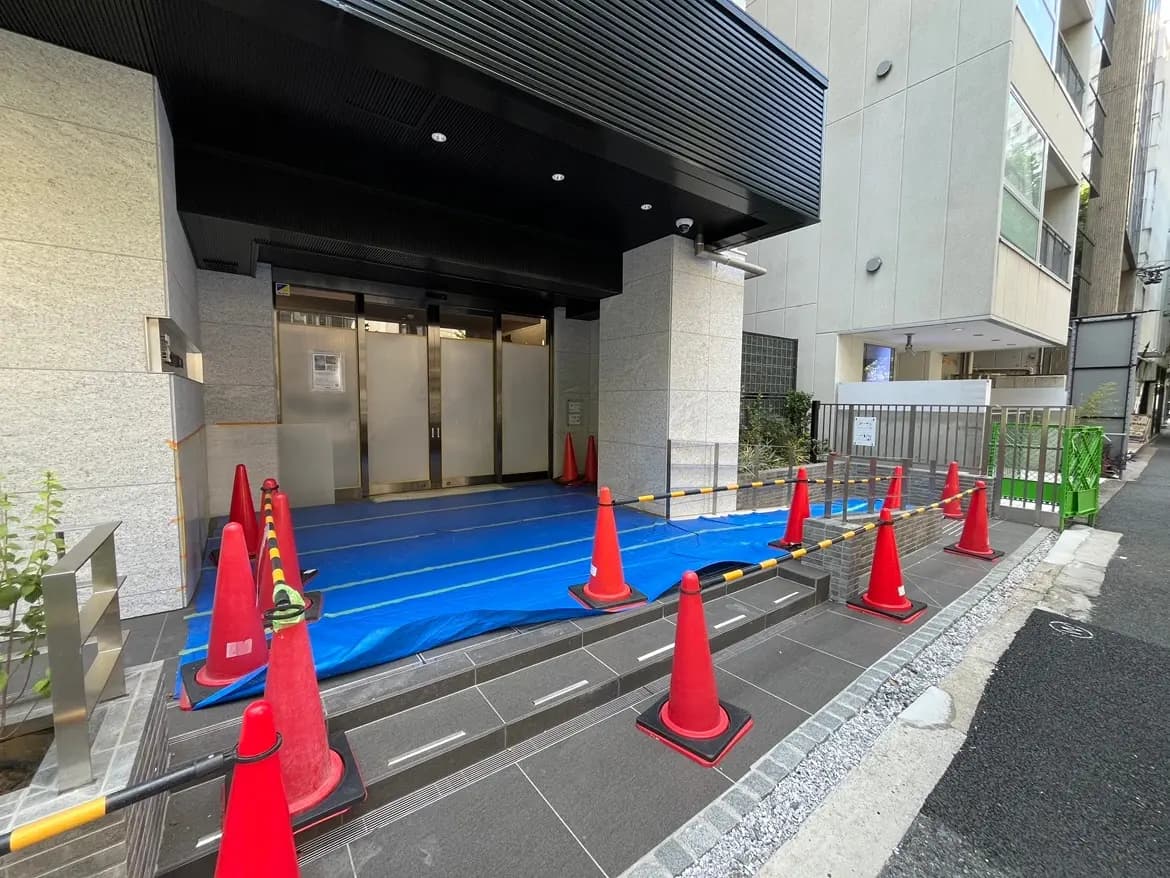 - 建物の入り口前に設置された赤いコーンと青いシート、安全対策のための遮断区域、周囲にある現代的な建築の一部