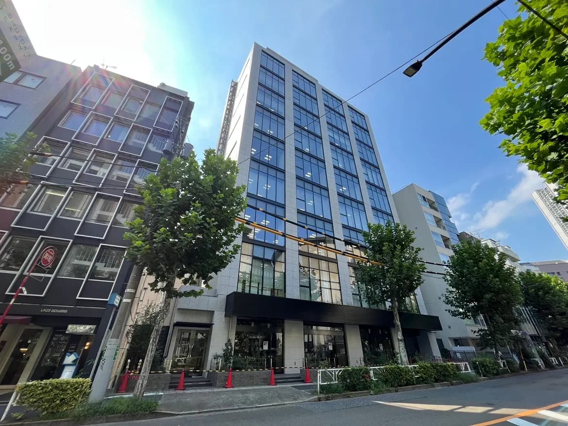 - モダンなオフィスビルの外観、ガラスのファサードと周囲の緑、青空が広がる繁華街の風景