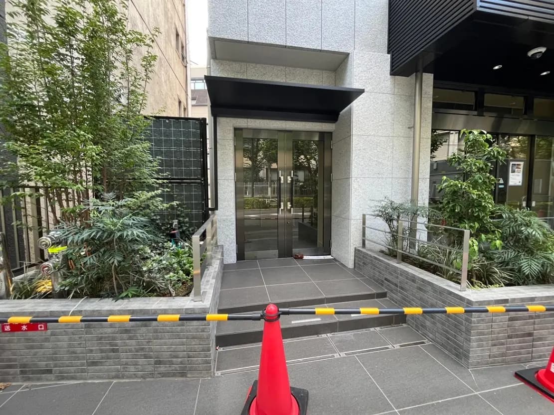- 現代的なビルのエントランス、植物がある緑溢れる景観と障害物を示すバリケードが設置された入口の様子