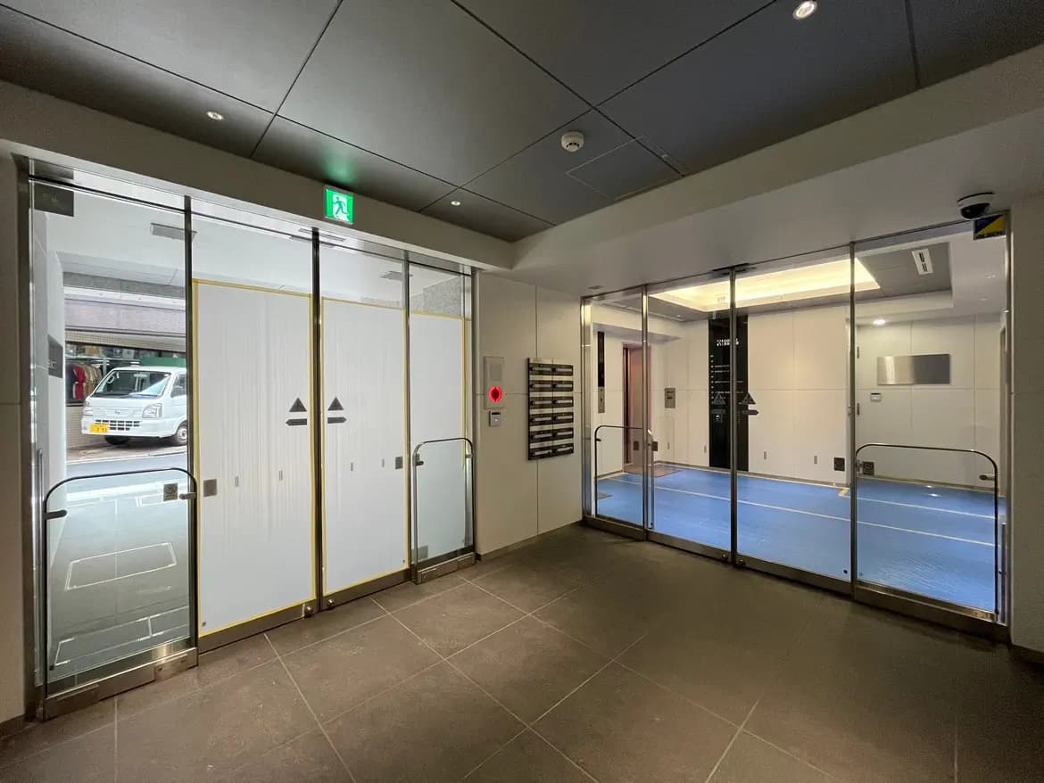 - 近代的なエントランスエリア、ガラスドアとホームドア、明るい照明が施されたデザイン、招待状ボックスとエレベーターの近く