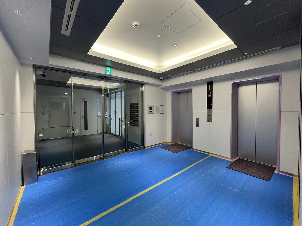 - モダンなビルのエレベーター前のロビー、ガラス扉と青いフロア、照明付きの天井デザイン