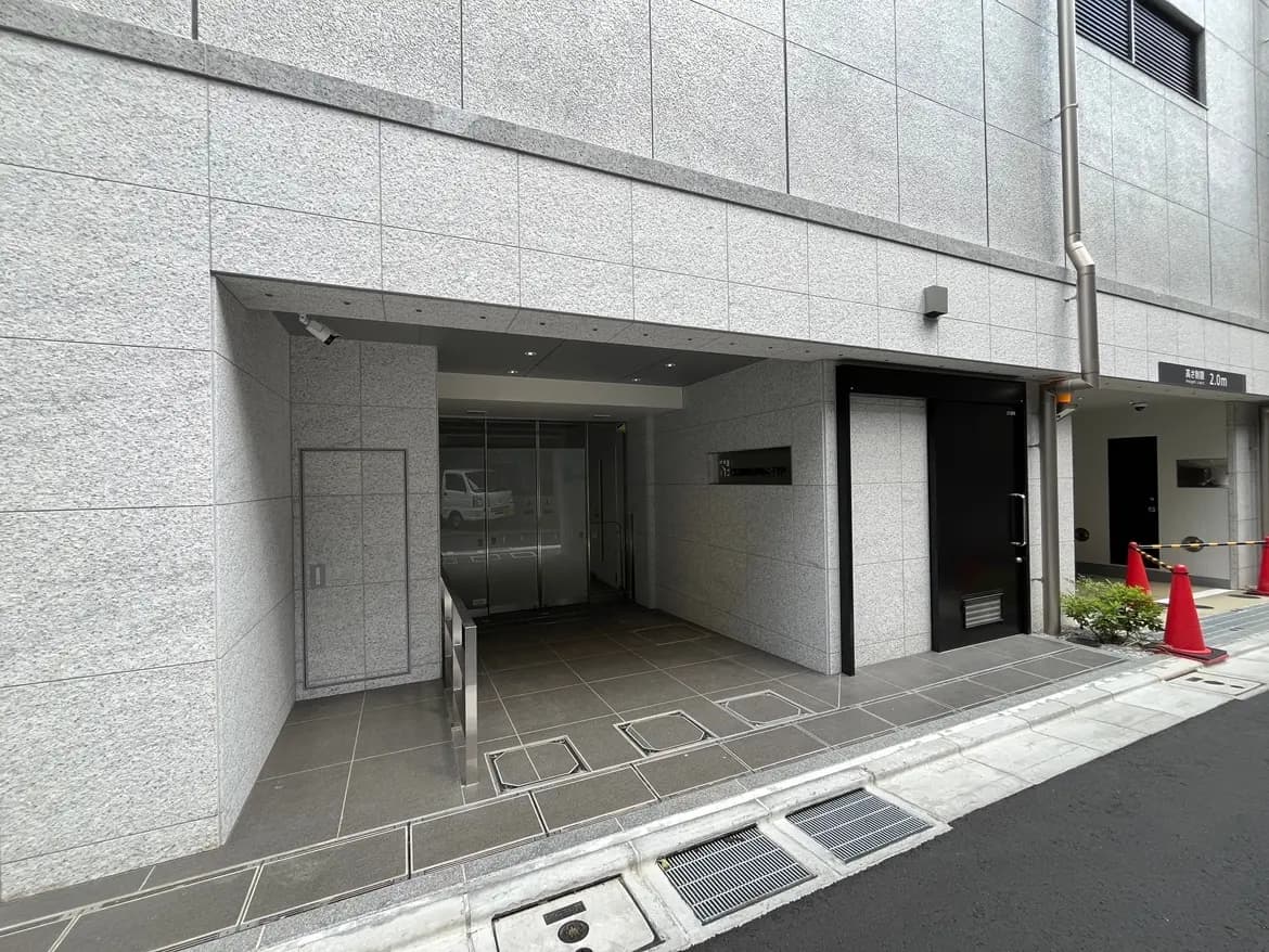 - モダンな外観のビルのエントランス、ガラスドアとスロープ、灰色のタイルで舗装された歩道が特徴の景観