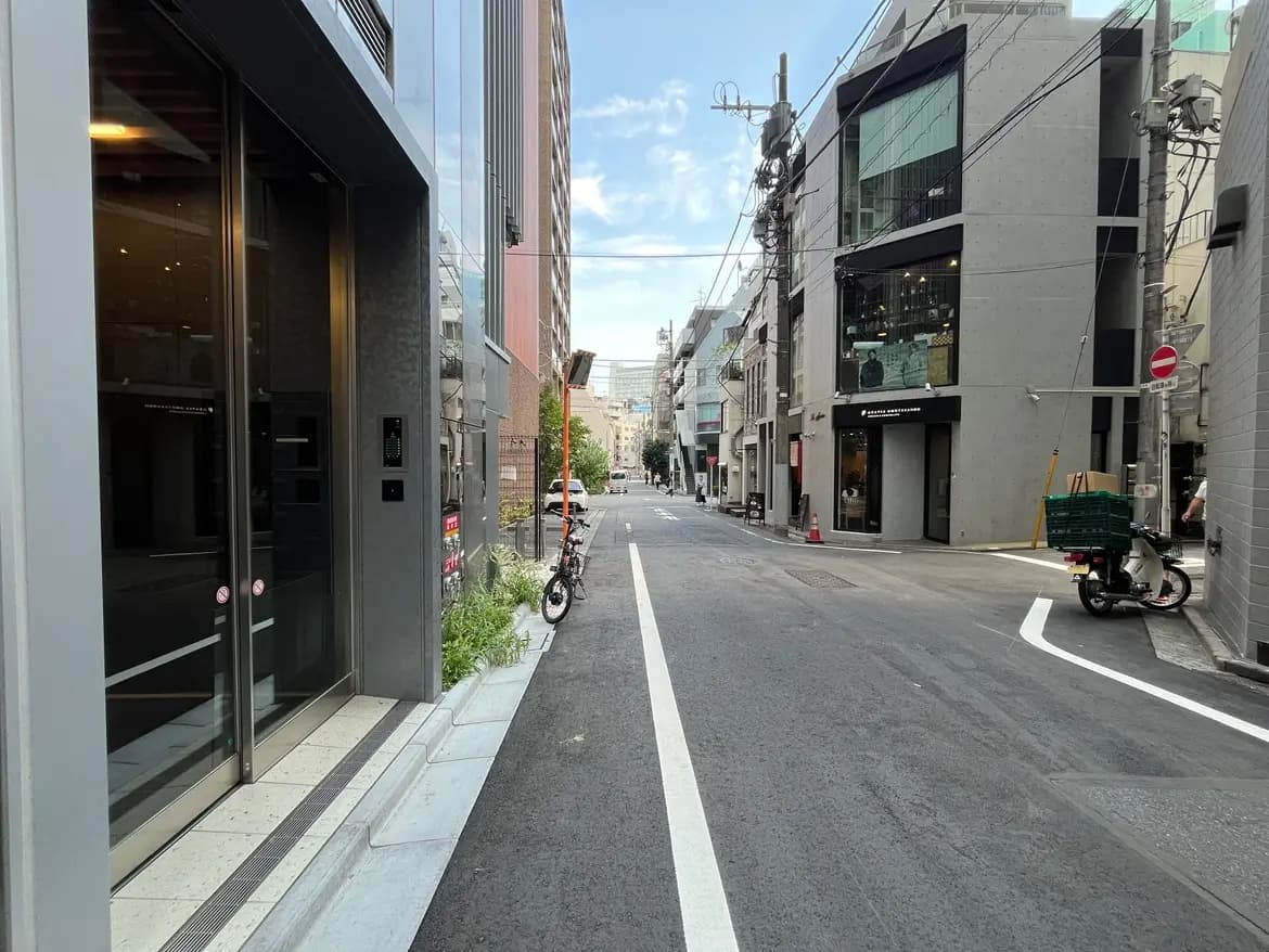 - 都会的な街道の風景、近代的なビルと商業店舗、駐輪場がある通り、青空と明るい日差しが広がるシーン