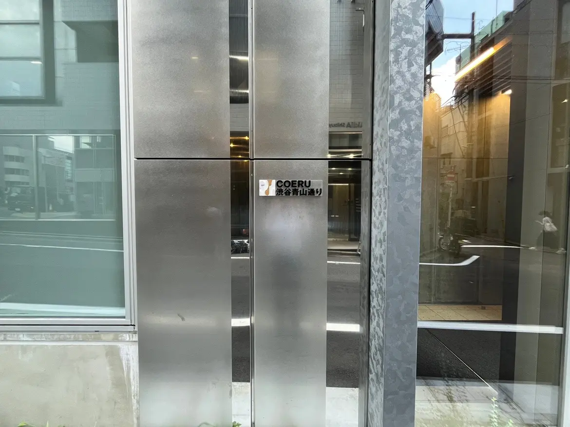 - 銀色の金属製の外観とガラスのエントランス、COERUの看板が掲げられたモダンなビルの入口