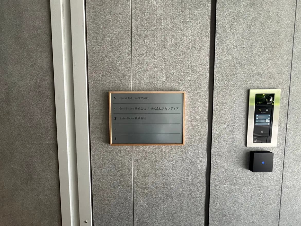 - 企業のエレベーター前に設置されたフロア案内板、シンプルなデザインと会社名が記載されたプレート