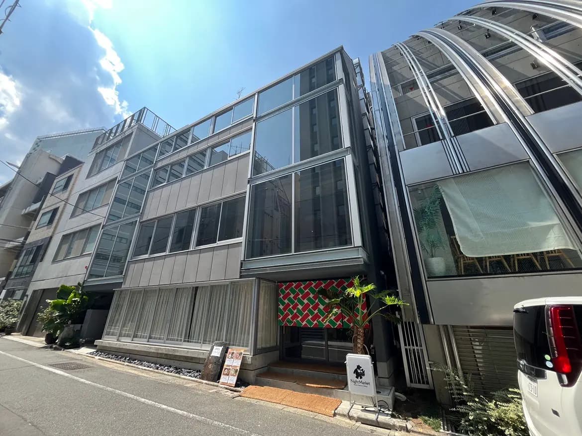 - ガラスと金属を使用したモダンな外観の建物、道路沿いに並ぶ飲食店の入り口と植栽が特徴的な景観