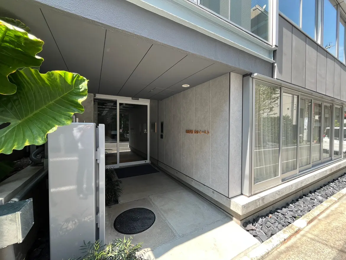 - モダンな建物のエントランス、広々とした入口に大きなガラスドアと緑の植物、清潔感のある外観