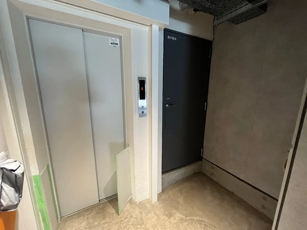 - エレベーターと玄関ドアが見える室内のコーナー、落ち着いた色合いの壁と床のデザイン