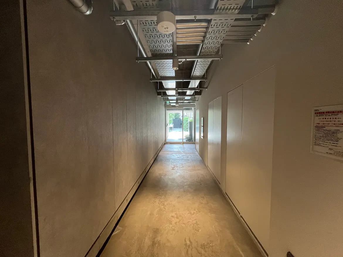 - 明るい光が差し込むモダンな廊下、シンプルな壁とフローリング、奥に透明なドアが見えるデザイン