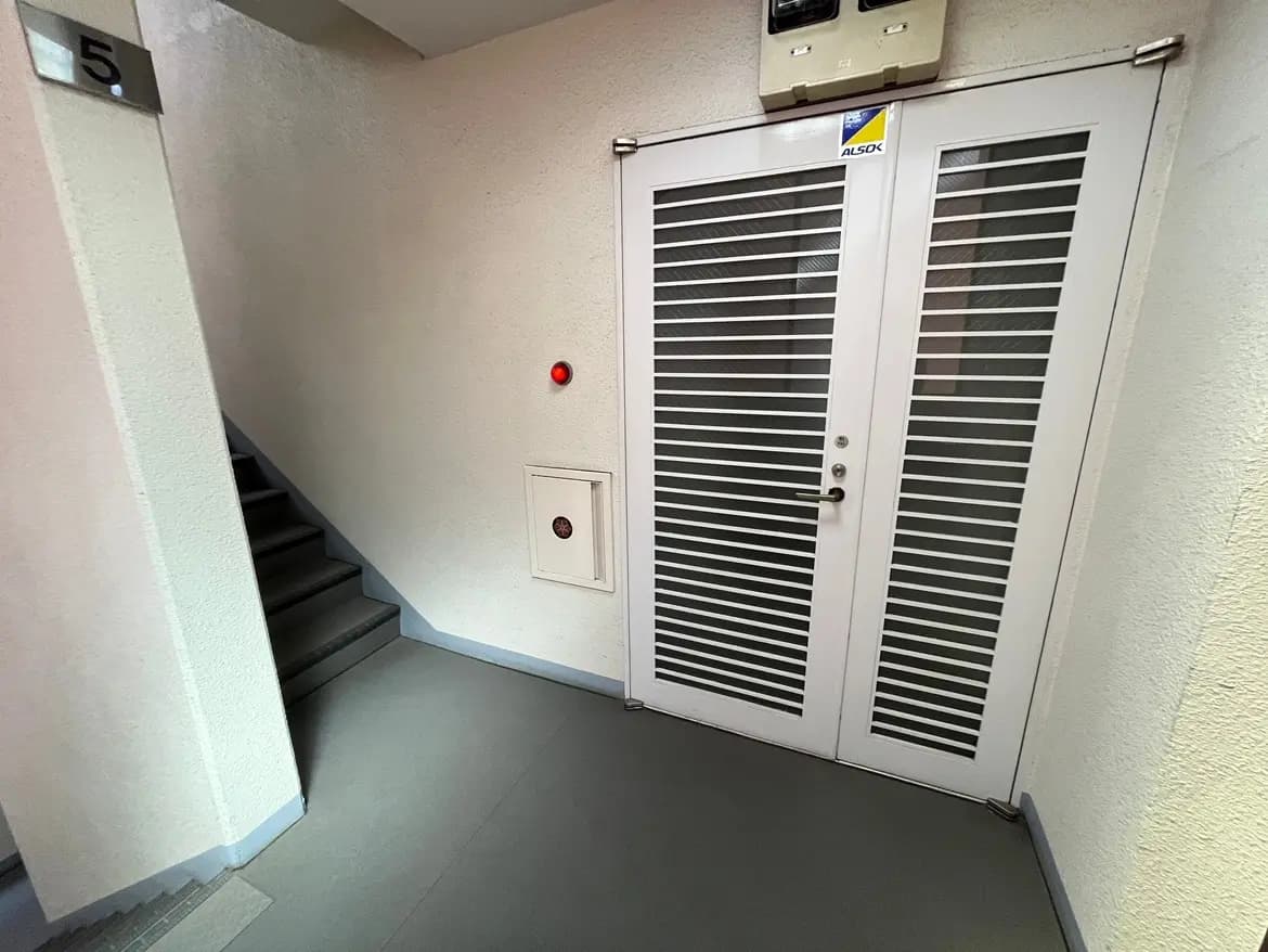 - 中階段の前にある白いスチールドア、横に配置された赤い警告灯とマンションの番号5が表示されたシンプルな廊下インテリア