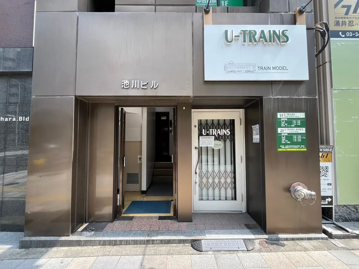 - 池袋のU-TRAINSビルの入り口、シンプルでモダンな外観、看板には「TRAIN MODEL」と書かれたデザイン