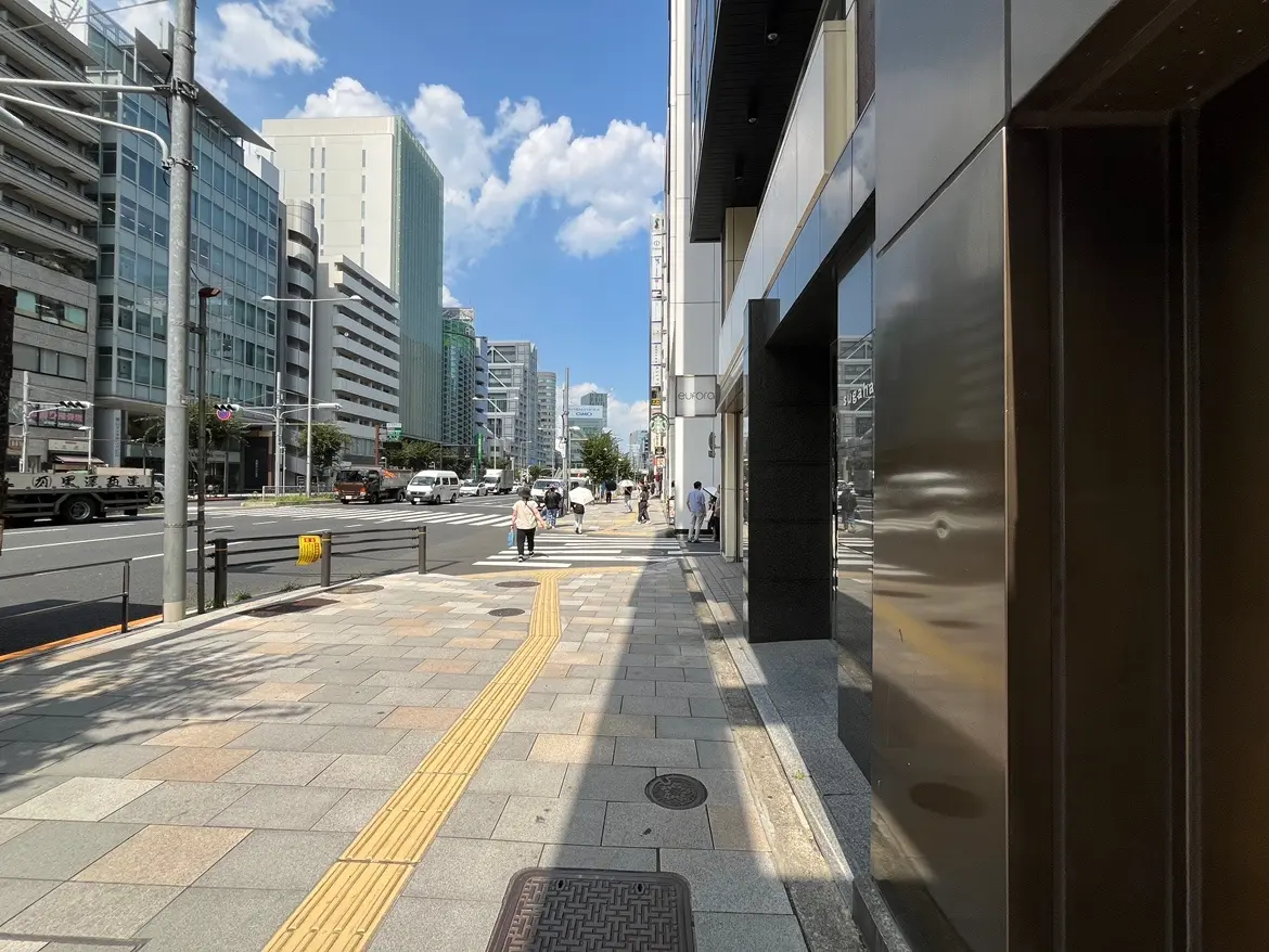 - 新しい街並みと高層ビル、青空の下で人々が歩く繁華街の様子、歩道と交通標識が写った風景