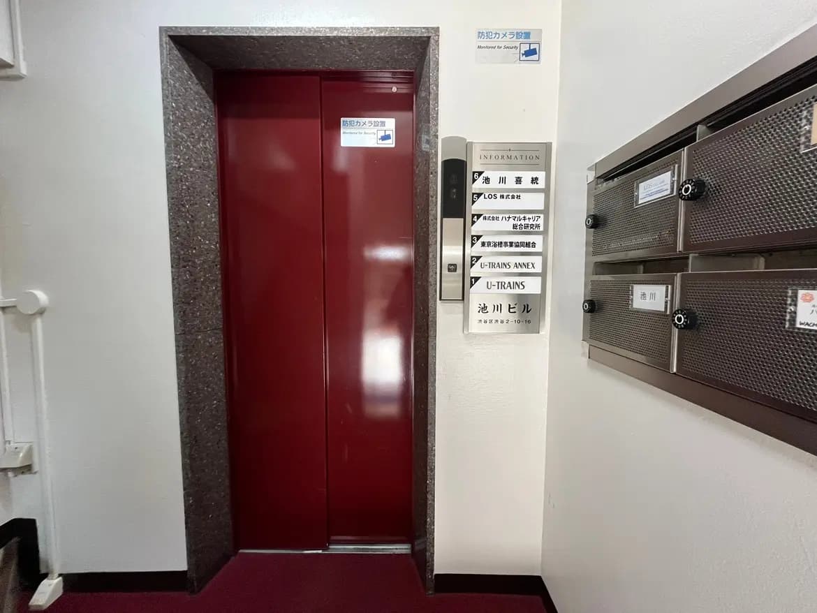 - 赤いエレベーターと案内板、隣にある郵便受けが並ぶ建物のエントランスホールの内部景観