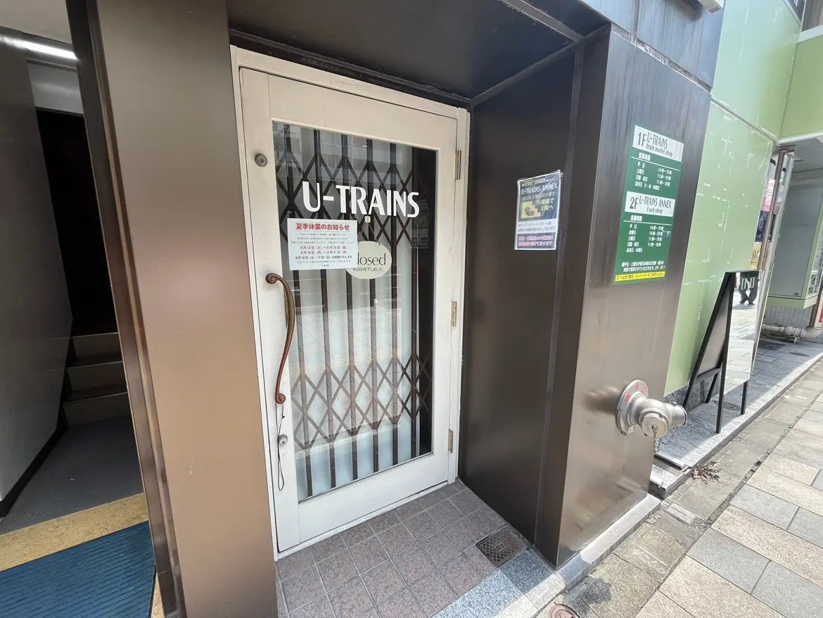 - 店名「U-TRAIN」の表示がある茶色の建物の入口、施錠されたドアと夏季営業のお知らせが掲示されたオシャレなデザイン