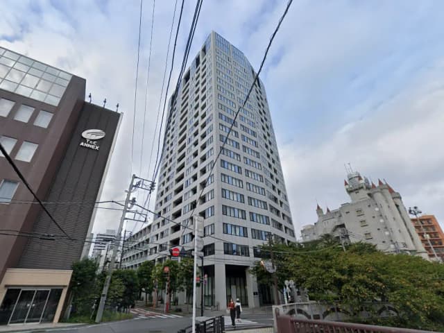 - TAC ANNEXと高層ビルが並ぶ都市の風景、道路脇に歩行者がいる様子、曇り空の背景