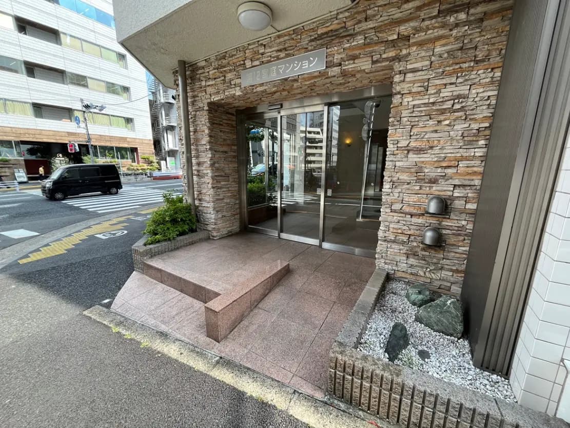 - モダンな外観のマンション入り口、石材の壁と広い階段、側道に面したデザインが特徴のエントランス