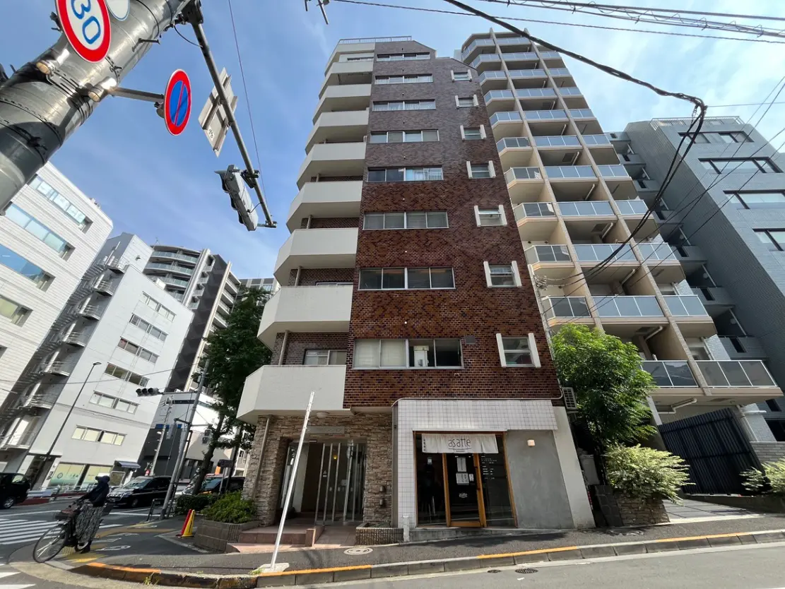 - 都会的な外観のマンション、レンガ調の壁と大きなバルコニー、周囲に高層ビルと交通標識が見える景観