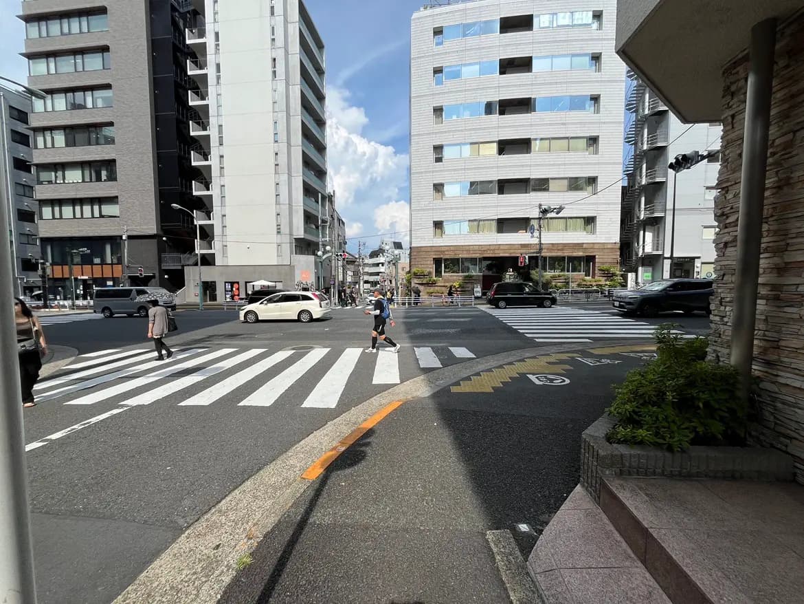 - 都会の交差点、白い横断歩道を渡る人々と周囲のビルが見える風景、晴れた青空の下の街並み
