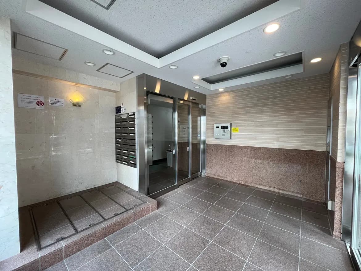 - 清潔感のある建物のエントランス、郵便受けと自動ドア、明るい照明とタイルの床が特徴の空間