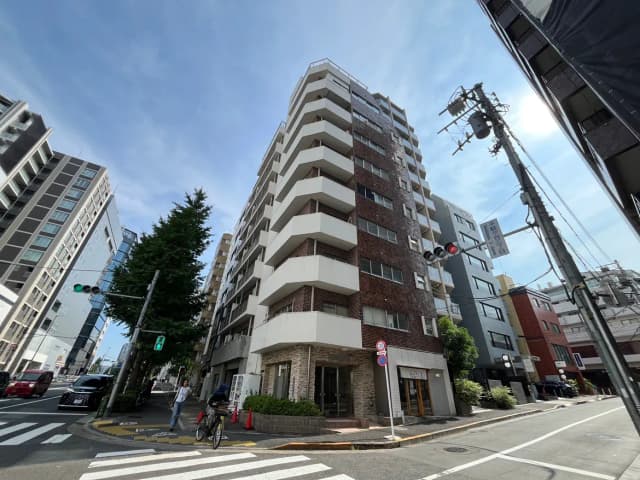 - 都市型マンションの外観、白とブラウンのタイル張り、青空と交差点の交通信号が見えるシーン