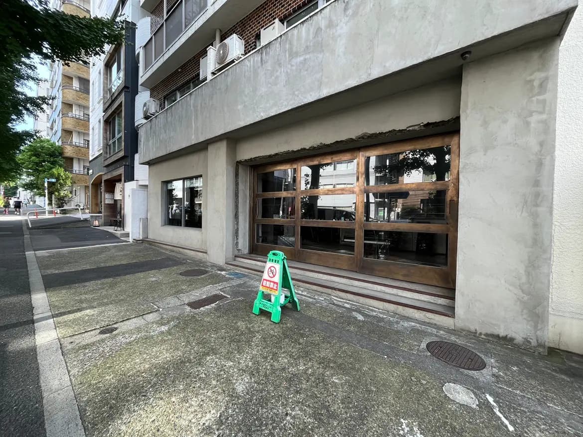 - 窓が大きく設計されたモダンな建物の外観、手前には緑色の標識が立っている歩道の様子