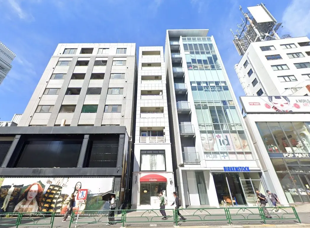 - 現代的なビル群が並ぶ都市の風景、一階に店舗があり、周囲には歩行者が行き交う賑やかな通り
