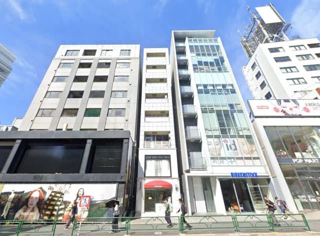 - 現代的なビル群が並ぶ都市の風景、一階に店舗があり、周囲には歩行者が行き交う賑やかな通り