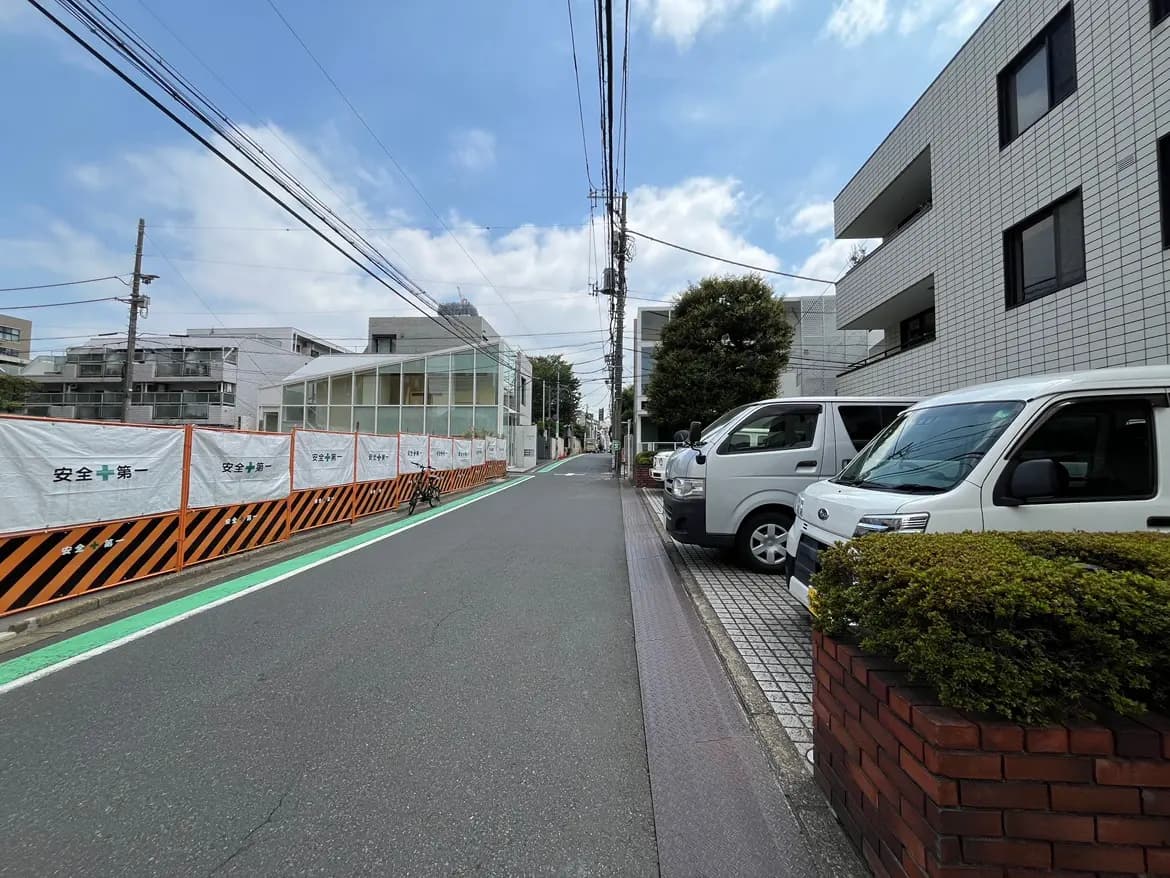 - 自転車が停まった静かな市街地の風景、工事中の柵と白い車が並ぶ道路沿いの様子