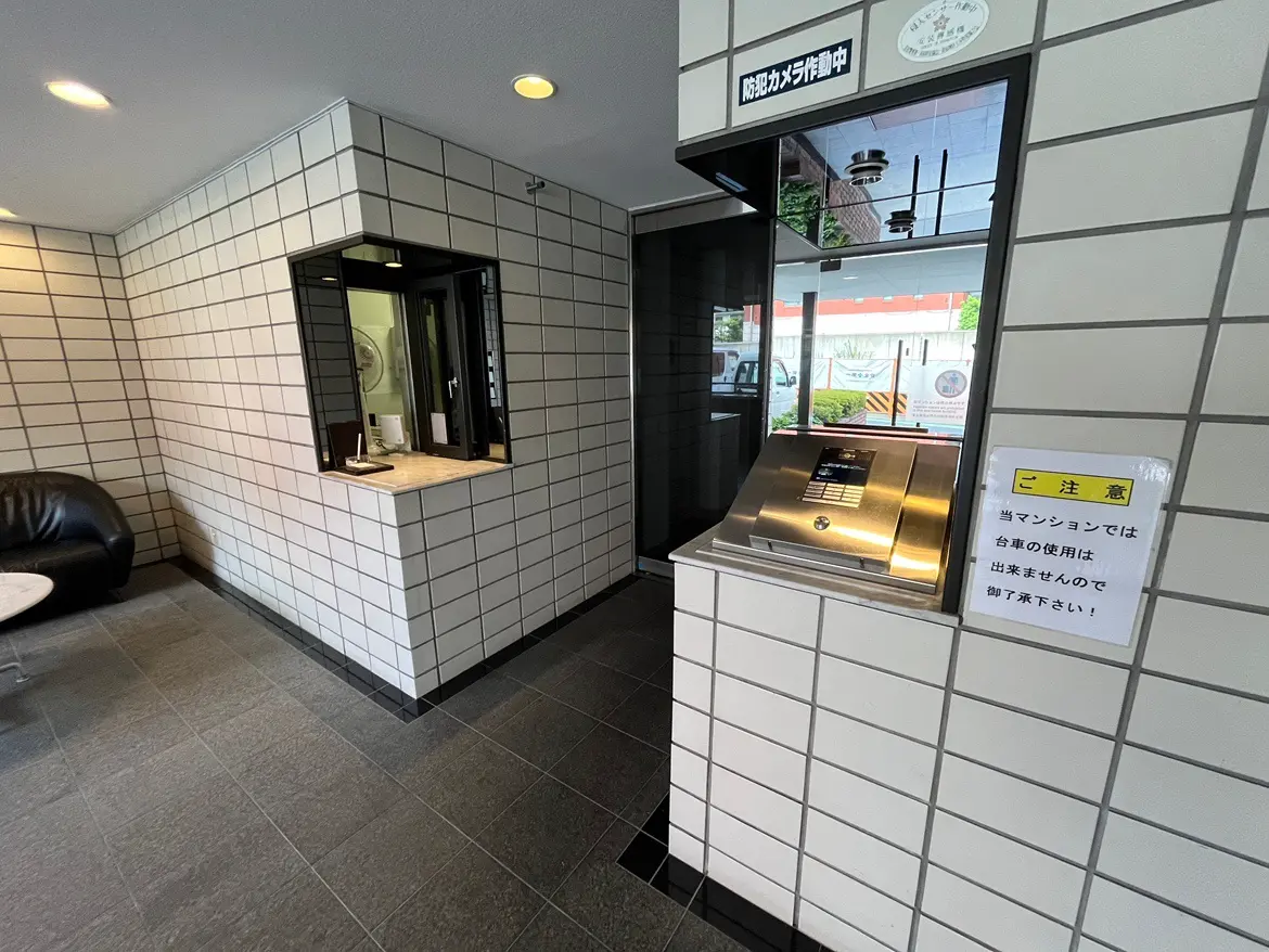- モダンなマンションのエントランス、壁タイルでデザインされた受付カウンターと注意書きが掲示された空間