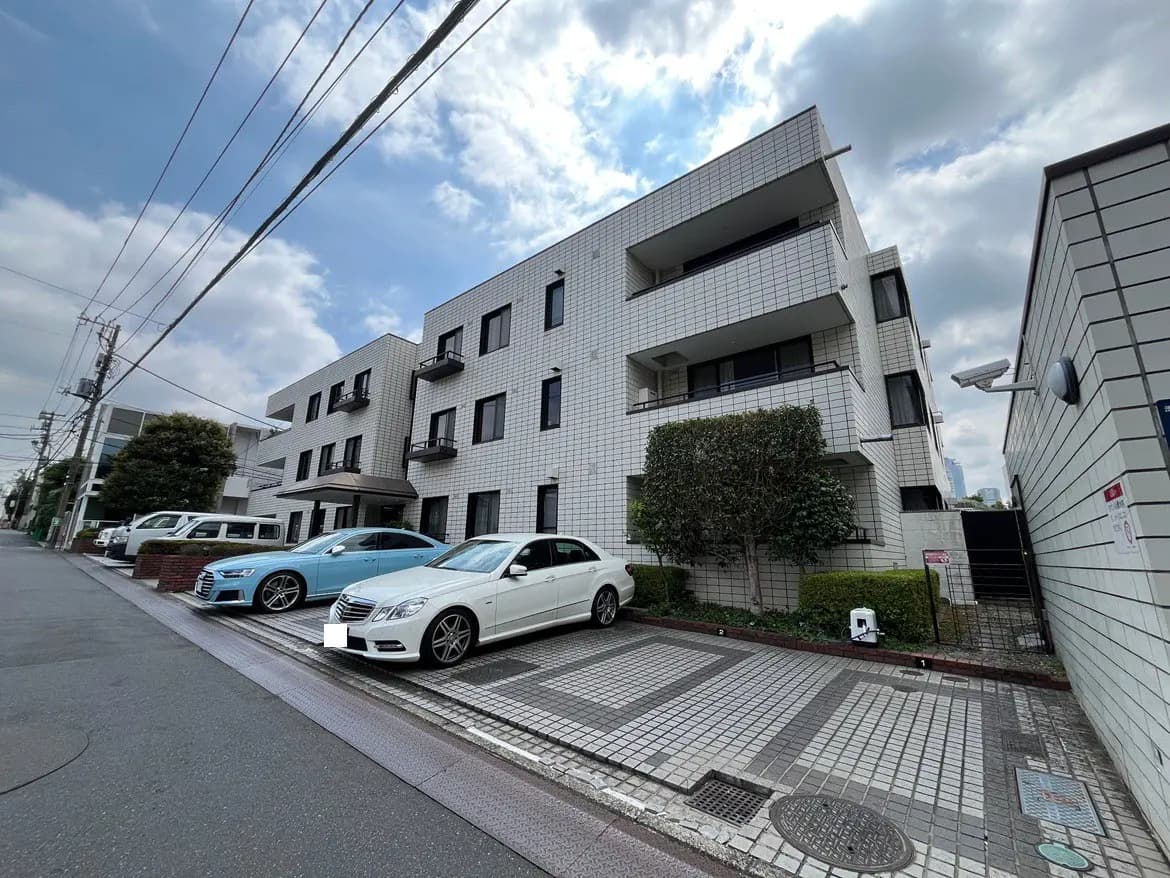 - モダンな外観のマンション、白いタイル張りの建物と整然と駐車された車、青空と雲の下での風景