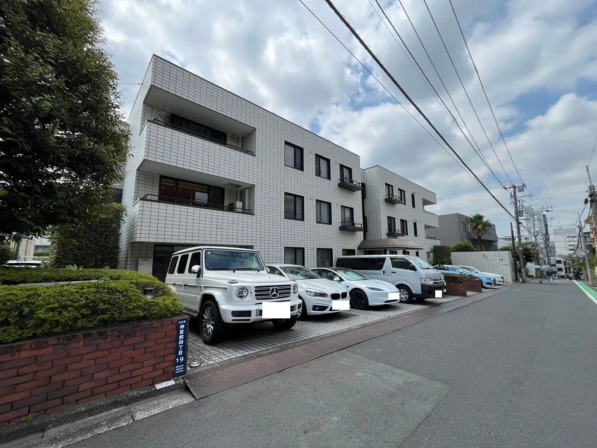 - 白いタイル張りの外観を持つマンション、周囲に駐車された複数の車両、晴れた空の下にある都市の風景