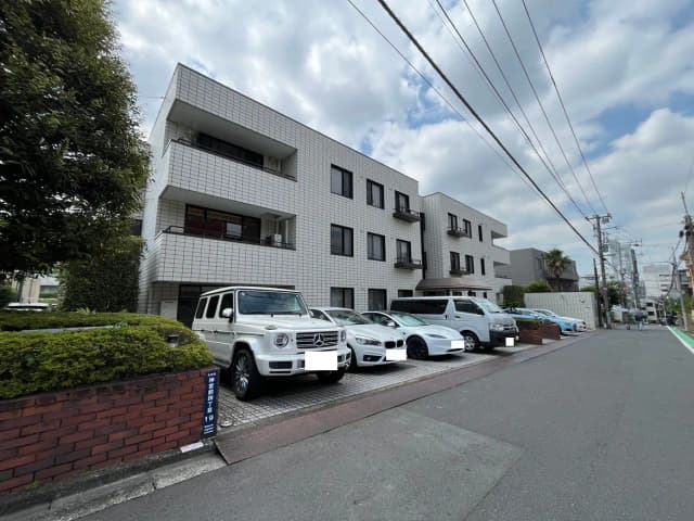 - 白いタイル張りの外観を持つマンション、周囲に駐車された複数の車両、晴れた空の下にある都市の風景