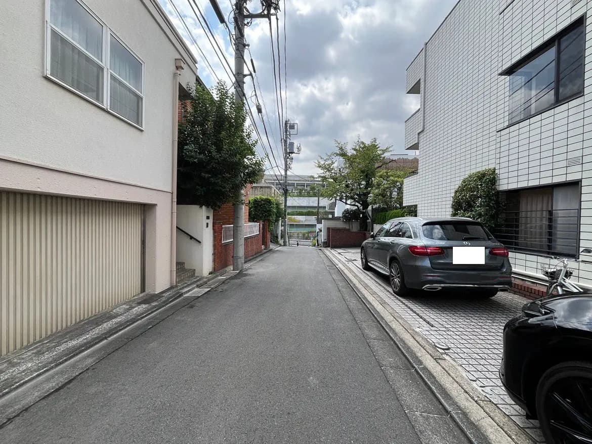 - 緑がある静かな住宅街の道路、隣接する家々と駐車された車が見える風景