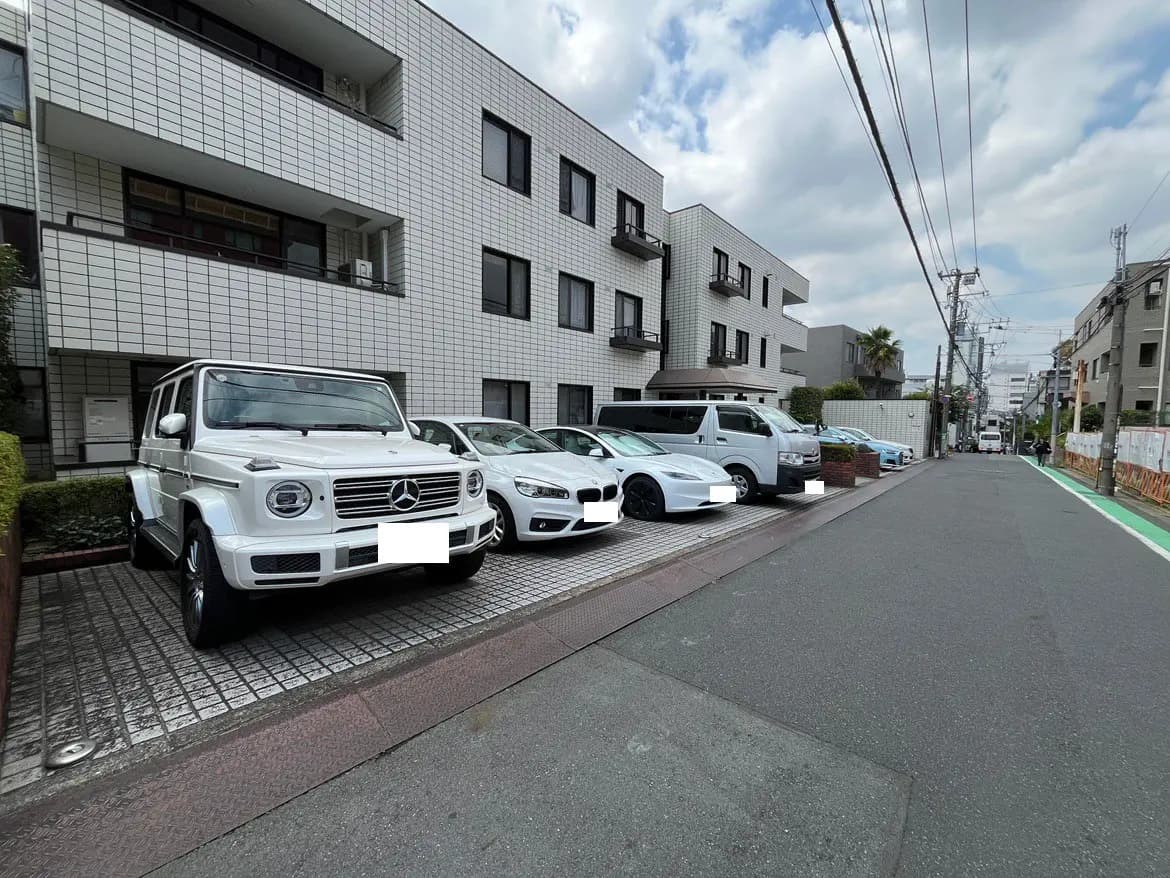 - 白いメルセデス・ベンツと様々な乗用車が停車している住宅街の風景、背後にはモダンなアパートメントの外観が見える景色
