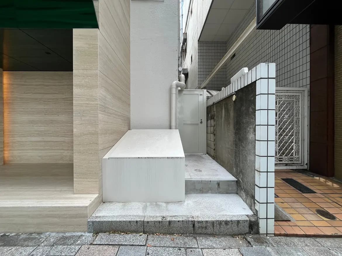 - 都会の一角にある石材の階段と白いディスプレイボックス、隣接する建物の壁と扉が映る風景