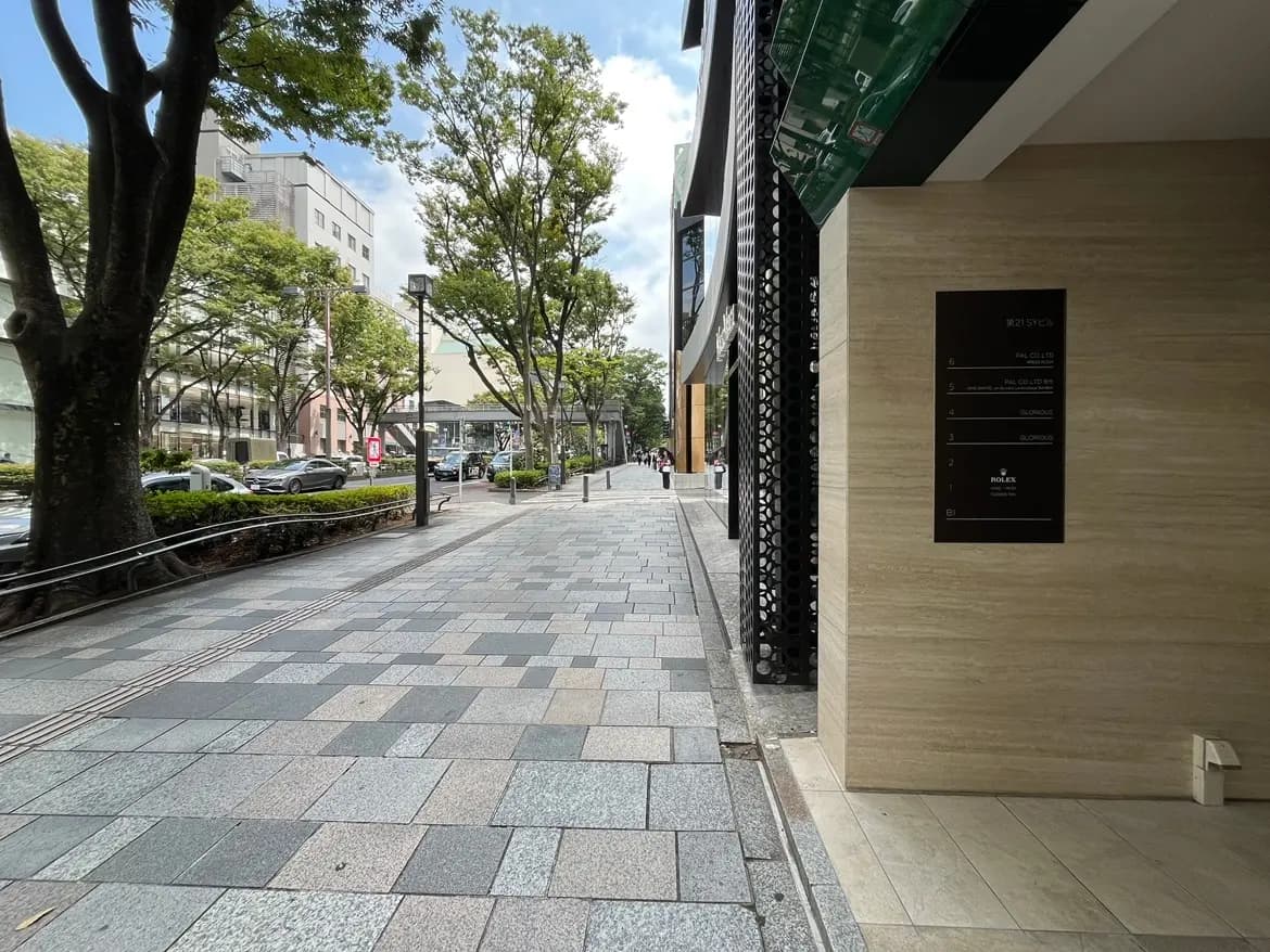 - 緑豊かな街並みと舗装された歩道、銀行や店舗が並ぶ通りの風景、近くには高級ブランドの看板が見える