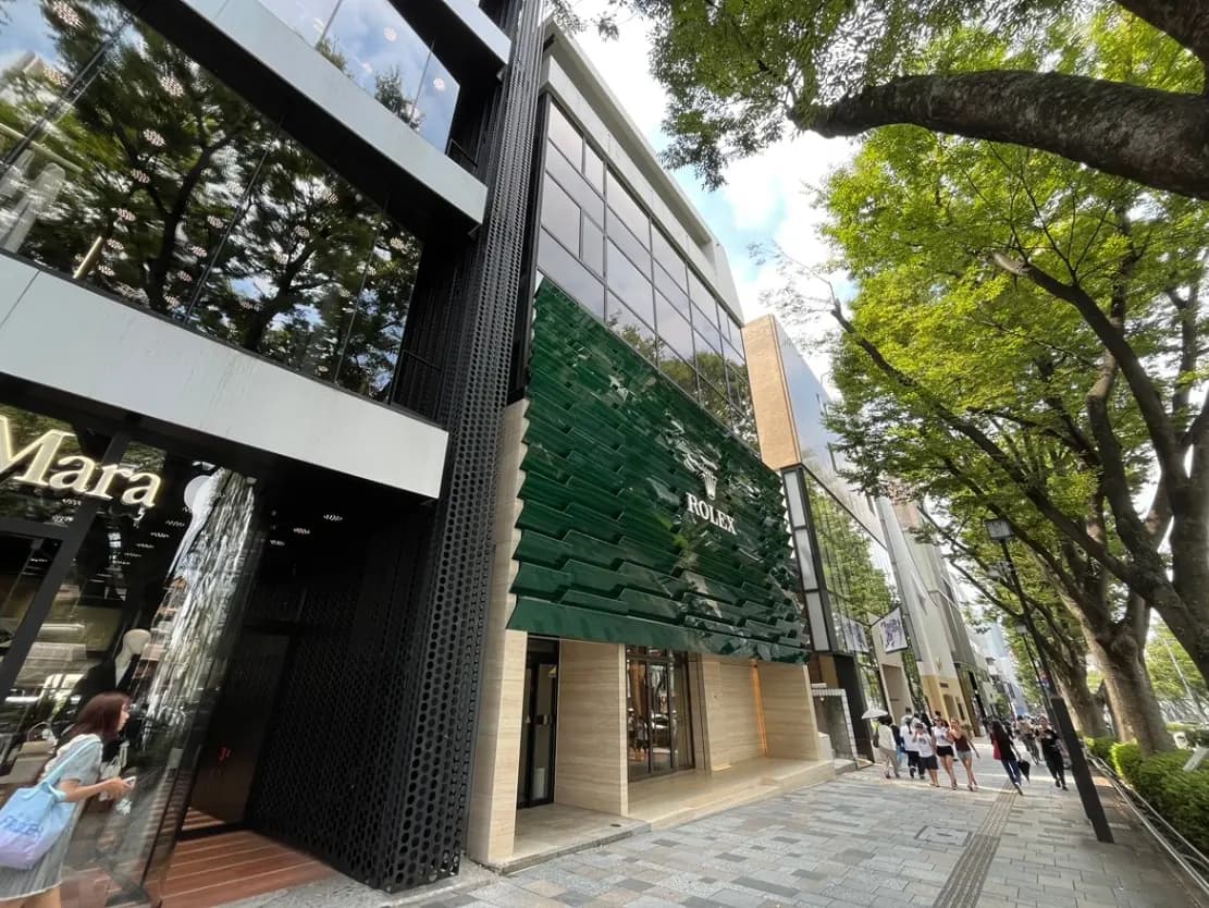 - 豪華なロレックスの店舗、モダンなファサードと緑の装飾、周囲には街並みや木々が広がる風景