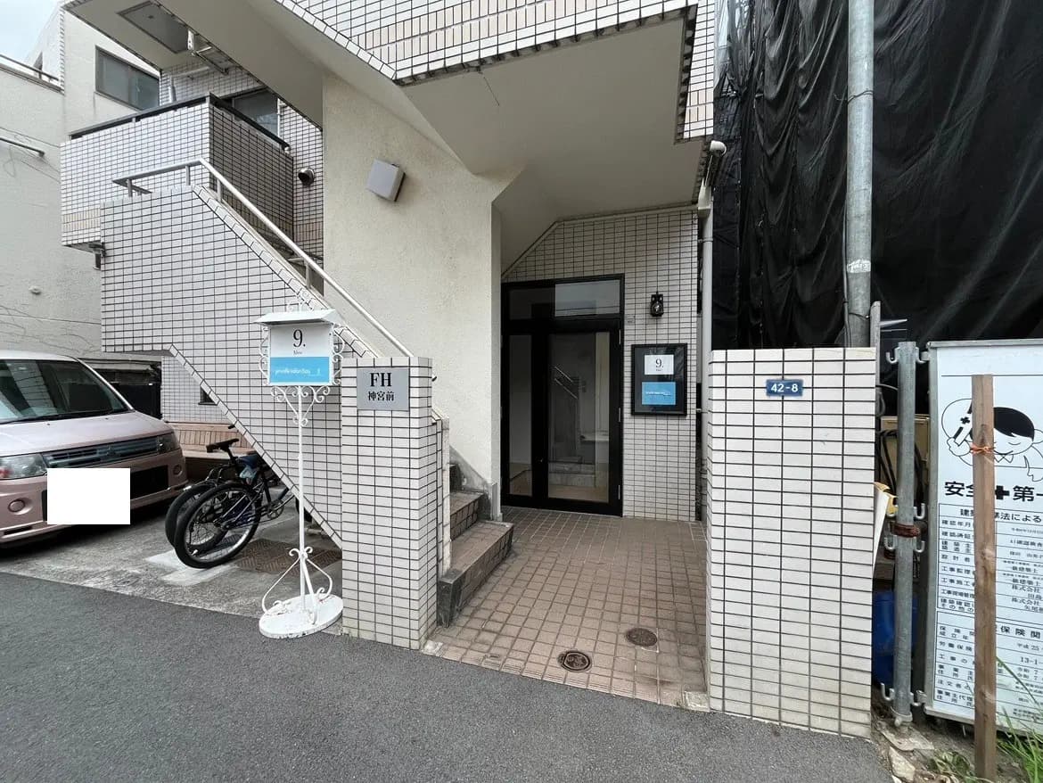 - 駐車場と自転車が置かれた白いタイルの外観、階段のあるアパートのエントランス周辺の風景