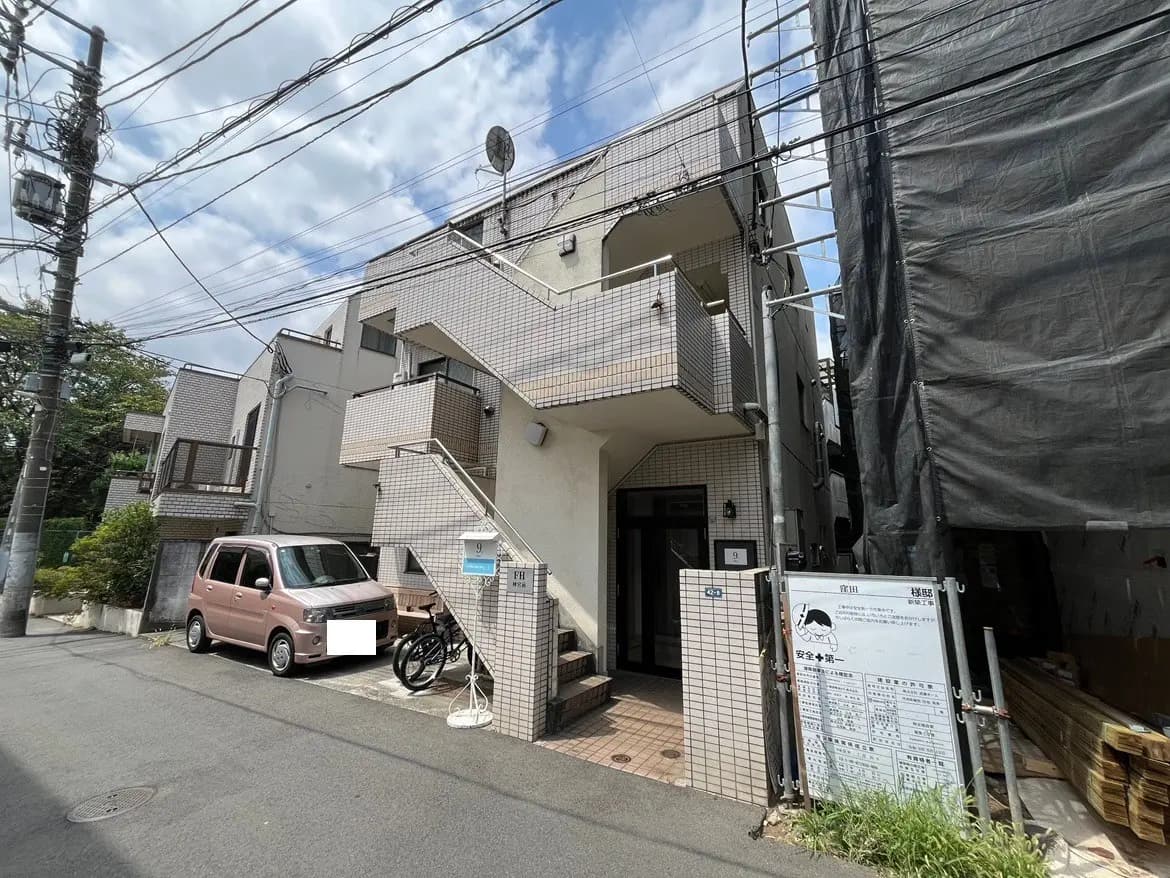 - 白い外壁のアパートメントビル、青空の下、駐車スペースにピンクの車と自転車を置いたシーン