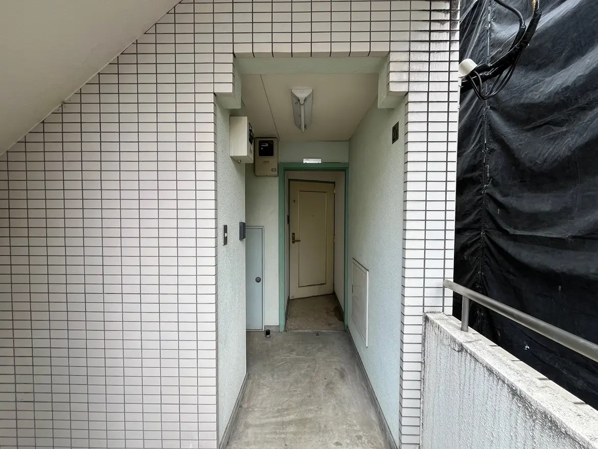 - タイル張りの壁とシンプルなエントランス、ドアと宅配ボックスが配置された廊下の内部の写真