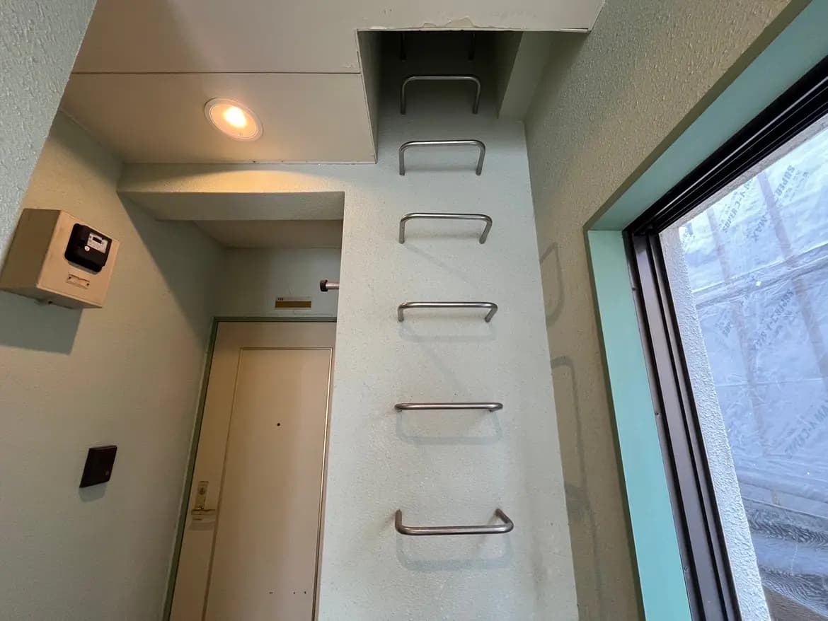 - 薄い緑色の壁を持つエントランスホール、金属製のラックが取り付けられた壁と明るい照明、窓から外の様子が見える画像