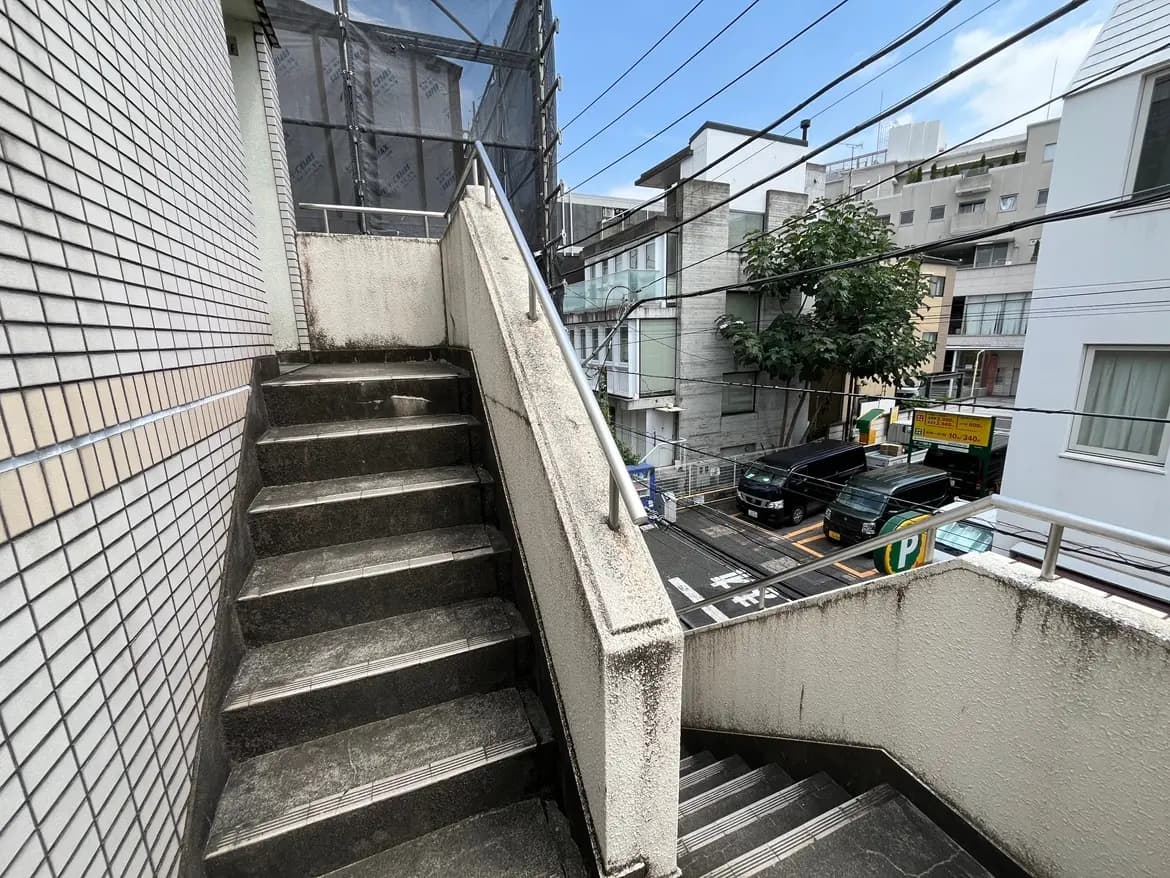 - 段差のある屋外階段、周囲の建物や道路が見える都市の風景、トーンの異なるタイルと手すりが特徴の空間