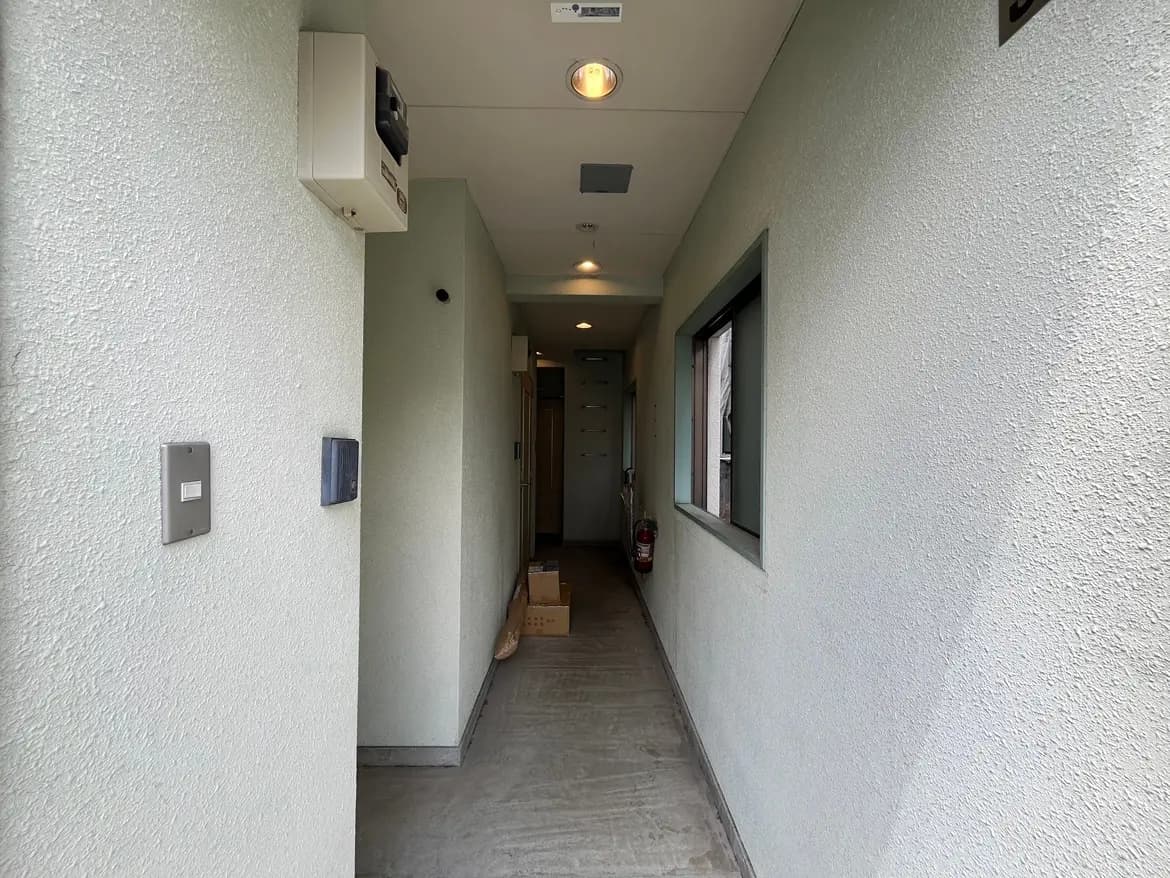 - 明るい照明が照らすシンプルなデザインの廊下、淡い色の壁と床、壁にはインターホンと消火器が設置されたインテリア